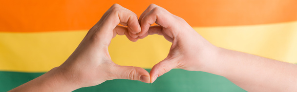panoramic shot of woman showing heart with hands on orange, yellow and green, human rights concept  - Foto, immagini