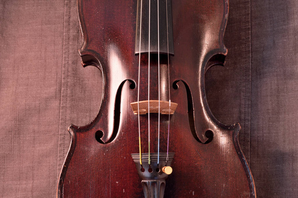 Old violin against gray seamed fabric. Violin is an antique from the early 1800's in a dark stain (original finish). - Photo, Image