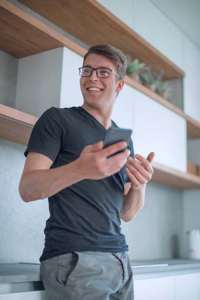 handsome guy with a Cup of coffee and a smartphone standing in the kitchen - Photo, Image