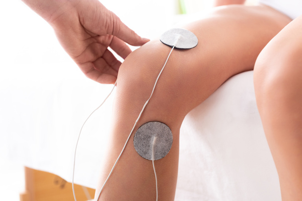 Terapistin beyaz arka planda hastanın dizine elektrotlar yerleştirmesi. - Fotoğraf, Görsel