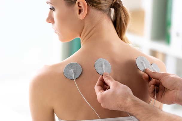 Terapeuta ustawienie elektrod na plecach pięknej kobiety podczas leczenia elektrodą - Zdjęcie, obraz