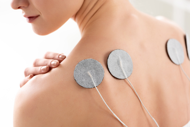 Vista ritagliata della schiena della giovane donna con elettrodi durante il trattamento degli elettrodi in clinica
 - Foto, immagini