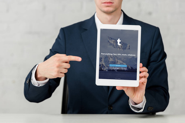 cropped view of realtor in suit pointing with finger at digital tablet with tumblr app on white  - Фото, изображение