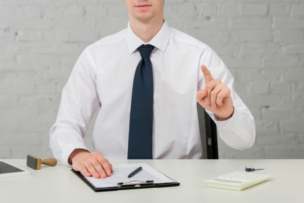 cropped view of realtor in suit pointing with finger while sitting at desk on white, leasing concept  - Fotoğraf, Görsel