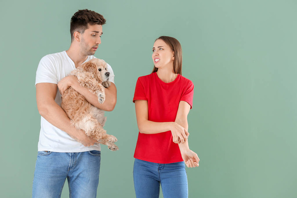 Young man with dog and his wife suffering from pet allergy on color background - Photo, Image
