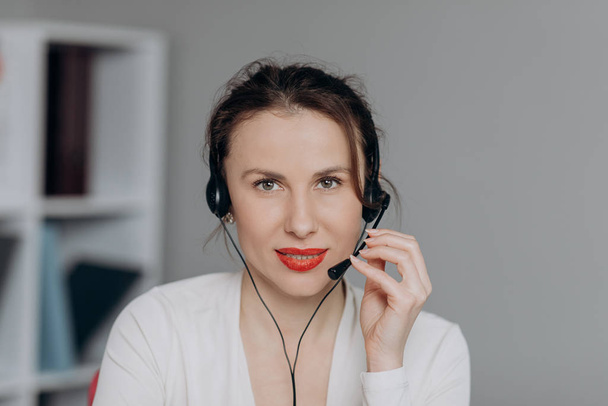 Young Smile Operator Working with a Headset and Happy Smile Face to the Camera. Young Beautiful Woman Operator with Phone Headset Looking at Camera and Smiling. - 写真・画像