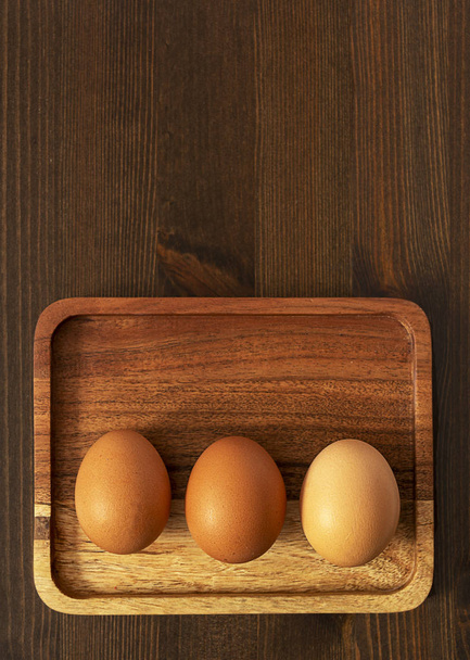 Three whole raw brown eggs on a light Board on a dark brown wooden background - Fotoğraf, Görsel