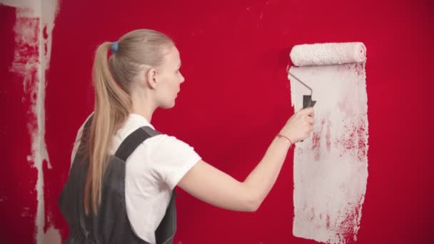 Μια γυναίκα βάφει έναν κόκκινο τοίχο με έναν λευκό κύλινδρο. - Πλάνα, βίντεο