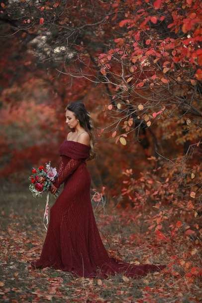 A woman a young bride in a red wedding dress with bare delicate shoulders holding a wedding bouquet - Фото, изображение
