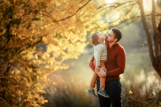 Ojciec młody mężczyzna trzyma córkę w ramionach i całuje ją na spacerze jesienią. - Zdjęcie, obraz