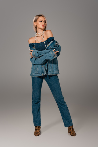 attractive woman in denim jacket and jeans looking away on grey background  - 写真・画像