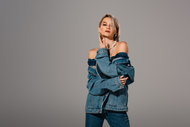 attractive woman in denim jacket looking at camera isolated on grey - Fotó, kép