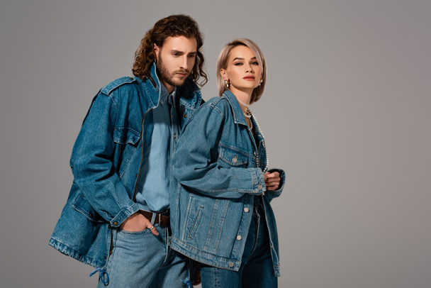 stylish man and woman in denim jackets looking at camera isolated on grey - Photo, Image
