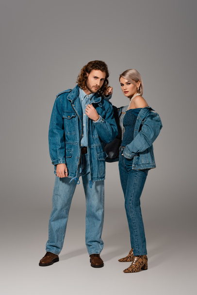 stylish man and woman in denim jackets and jeans looking at camera on grey background  - Foto, Imagem