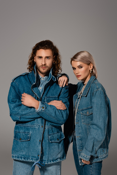 stylish man with crossed arms and woman in denim jacket looking at camera isolated on grey - Foto, afbeelding