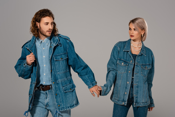 stylish man and woman in denim jackets holding hands isolated on grey - 写真・画像