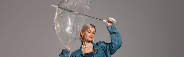 panoramic shot of attractive woman in denim jacket holding umbrella isolated on grey - Фото, зображення