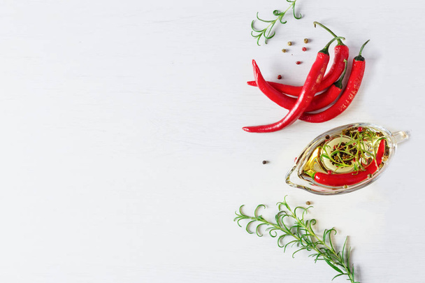 Olaj chilis fűszerrel és gyógynövényekkel. Friss chili paprika és rozmaring felső nézet fehér háttér. - Fotó, kép