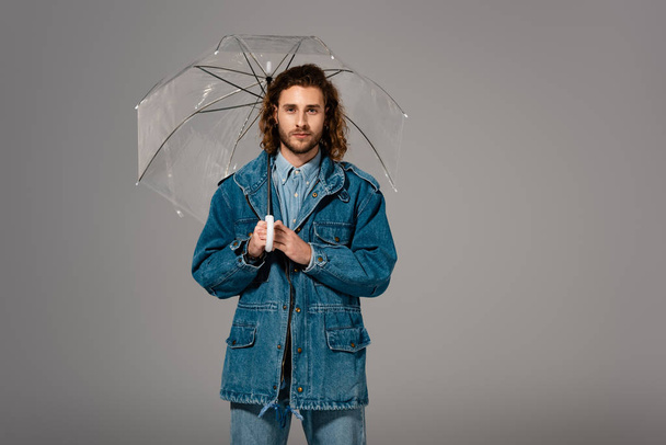 hombre guapo y elegante en chaqueta de mezclilla con paraguas aislado en gris
 - Foto, Imagen