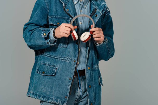 cropped view of stylish man in denim jacket holding headphones isolated on grey - Фото, изображение