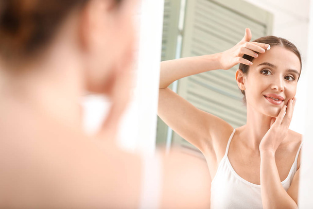 Beautiful young woman applying facial cream in front of mirror - Foto, Bild