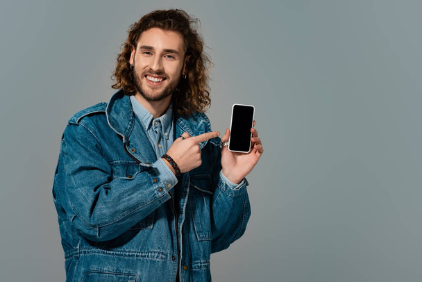 mosolygós férfi farmerdzsekiben ujjal mutogatva okostelefonra elszigetelt szürke - Fotó, kép