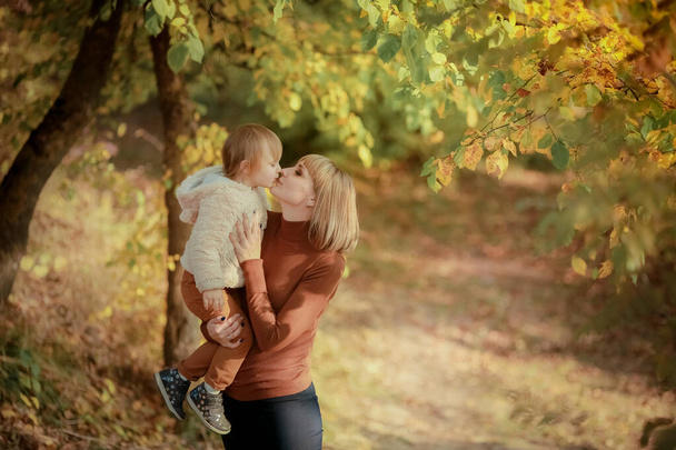 Autumn walk of a family of two. Mother and daughter in autumn Park with yellow falling leaves - Photo, Image