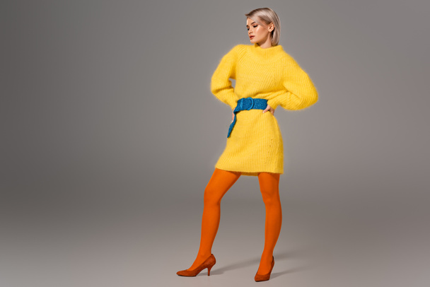 atractiva mujer en vestido amarillo con las manos en las caderas sobre fondo gris
  - Foto, imagen