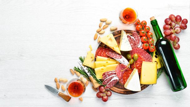 Italian antipasti wine snacks set. Cheese variety, salami and grapes on a white wooden background. Italian cuisine. Top view. Free space for your text. - Fotó, kép