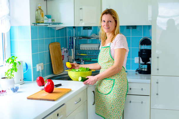blond woman standing in the kitchen with vegetables in a bowl - Foto, immagini