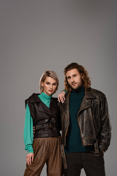 woman in vest and man in leather jacket looking at camera isolated on grey - Fotografie, Obrázek