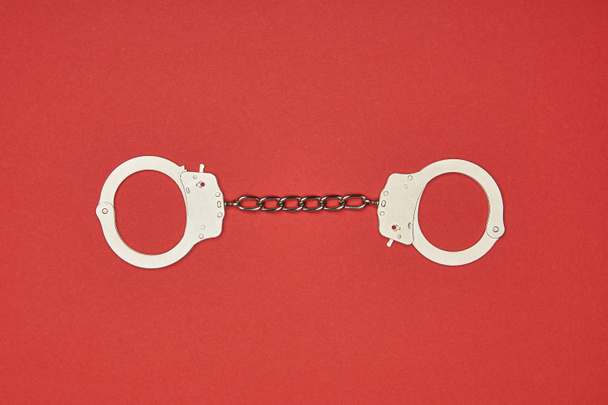 top view of metal handcuffs isolated on red - Foto, Imagem