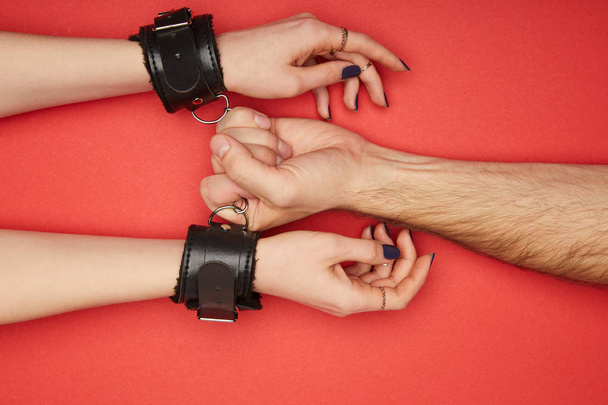 cropped view of man holding handcuffs on woman isolated on red - 写真・画像