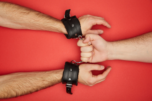 cropped view of man holding handcuffs on man isolated on red - Foto, Imagen
