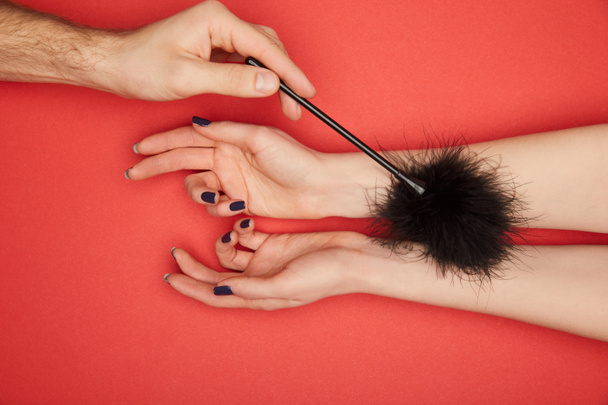 cropped view of man tickling female hands with feather tickler isolated on red - Photo, Image