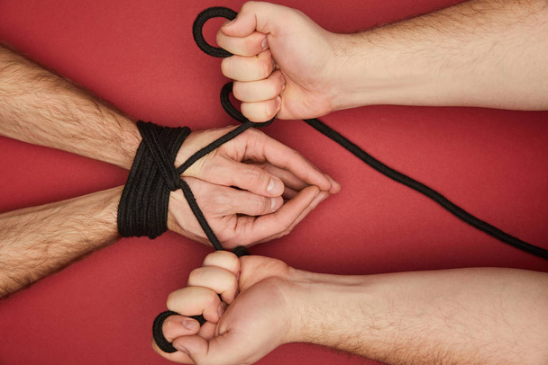 обрезанный вид человека, держащего веревку на связанных руках бойфренда изолированы на красный
 - Фото, изображение