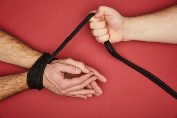 обрізаний вид людини, що тримає мотузку на зв'язаних руках хлопця ізольовані на червоному
 - Фото, зображення