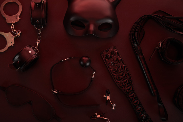 bovenaanzicht van seksspeeltjes in donker licht op rode achtergrond - Foto, afbeelding