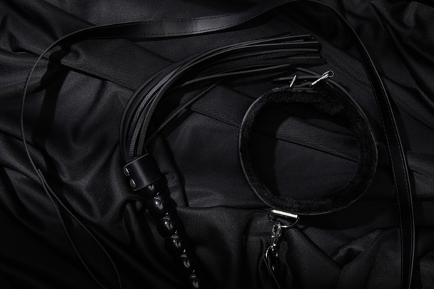 top view of leather flogging whip and collar on black textile background - Fotografie, Obrázek