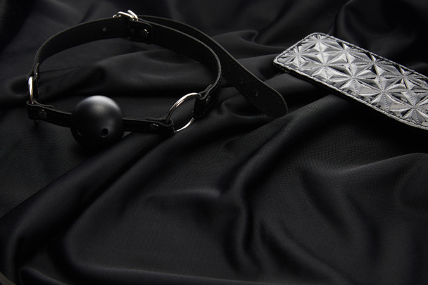 gag and spanking paddle on black textile background - Fotó, kép