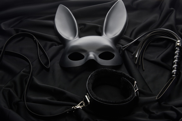 rabbit mask and sex toys on black textile background - Foto, afbeelding