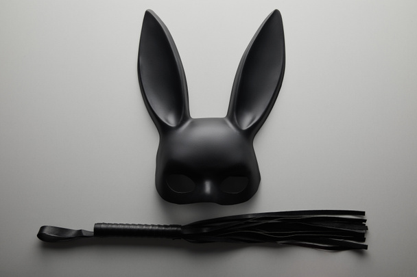 top view of black rabbit mask and flogging whip on white background - Photo, Image