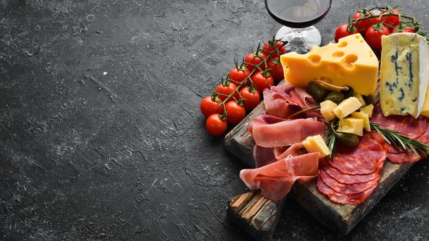 italian antipasti snacks, cheese and wine in glasses. Top view. On a black stone table. Free space for your text. - Zdjęcie, obraz