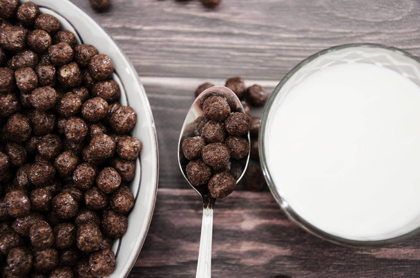 chocolate balls in a plate and a glass of milk. dry breakfast on a wooden background. Close-up. - Foto, afbeelding
