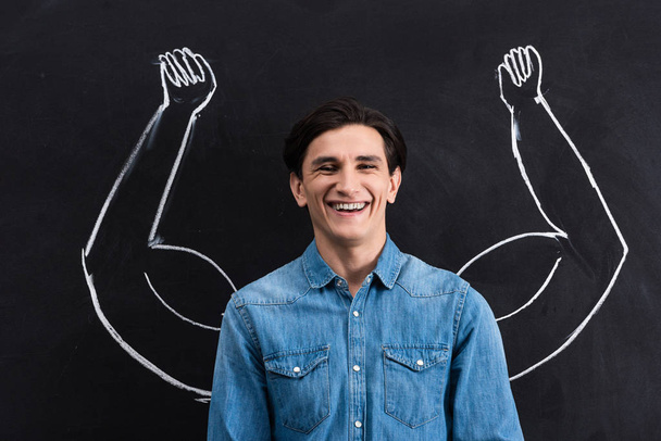 handsome smiling man with strong arms drawing on blackboard - Foto, Bild