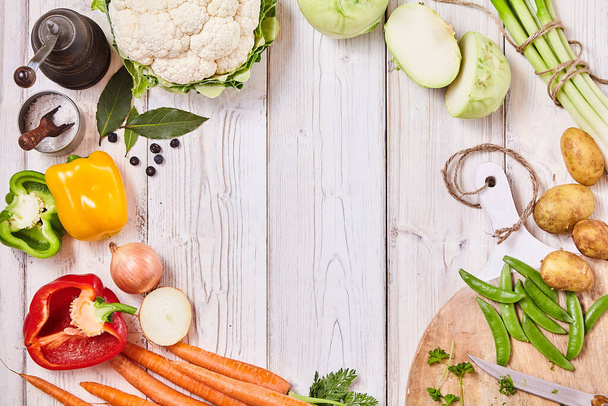 Deliciosas verduras frescas formando un marco en madera blanca con espacio de copia central junto con una tabla de cortar, cuchillo y condimento para cocinar
 - Foto, imagen