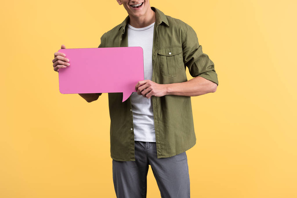 cropped view of happy man holding pink speech bubble, isolated on yellow - Fotó, kép