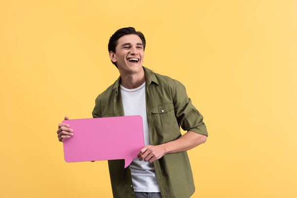 cheerful man holding pink speech bubble, isolated on yellow - 写真・画像