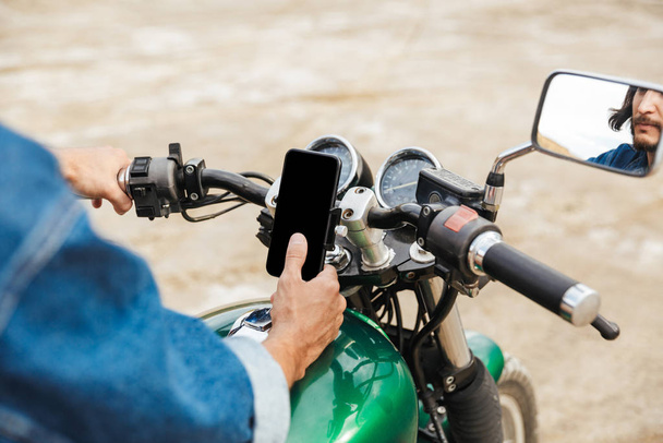 Close up of a man holding handle bars and using mobile phone - Zdjęcie, obraz