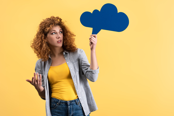 skeptical woman looking at empty speech bubble in shape of cloud, isolated on yellow  - Photo, Image